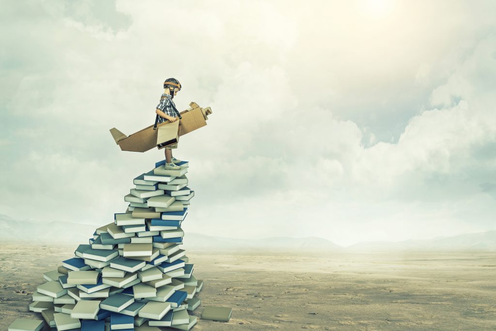 A kid with a cardboard plane on top of books 